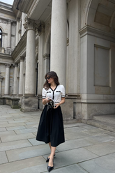 a lady in a white knit top with black trim and a black skirt